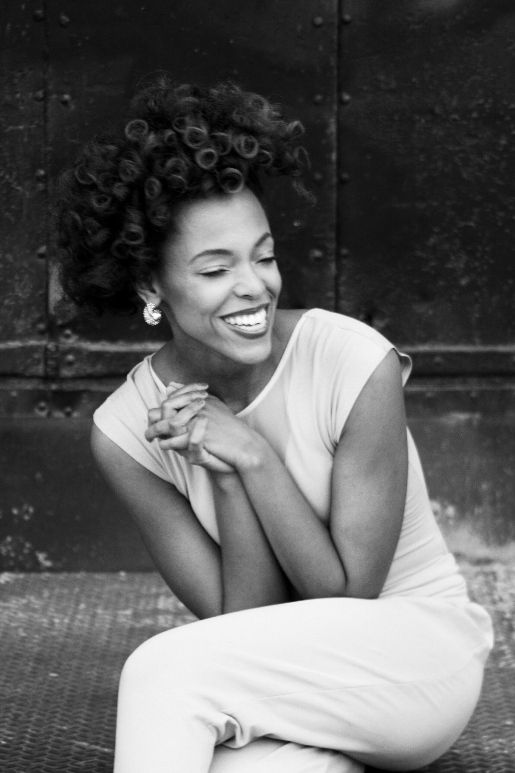 A black and white photo of Jillian Walker smiling with her eyes closed and hands clapsed.